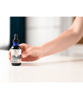 Hand holding Fulvic Ionic Minerals X350 bottle on a white countertop, showcasing its compact size and convenient dropper design.