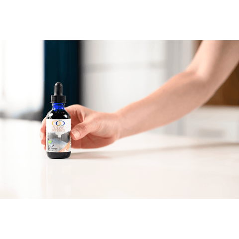 Hand holding Fulvic Ionic Minerals X350 bottle on a white countertop, showcasing its compact size and convenient dropper design.