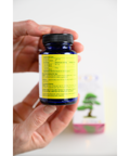 Hands holding a blue bottle of Red Pine Needle Oil Capsules with visible nutrition facts. Vegan supplement for skin and immune health.