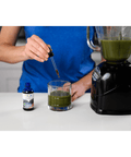 Person adding Fulvic Ionic Minerals X350 drops to a green smoothie, showcasing its compatibility with various health drinks.