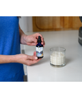 Person holding Fulvic Ionic Minerals X350 bottle next to a glass of milk, illustrating its adaptability for different beverages.