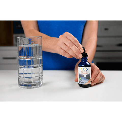 Person using the dropper from Fulvic Ionic Minerals X350 bottle to prepare a glass of water, highlighting its simple application process.