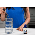 Woman adding Fulvic Ionic Minerals X350 drops into a glass of water, demonstrating easy usage for daily health supplementation.