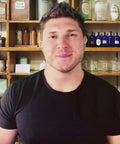 Man standing in front of vintage apothecary shelves, promoting Fulvic Ionic Minerals X350 by Optimally Organic for health and wellness.